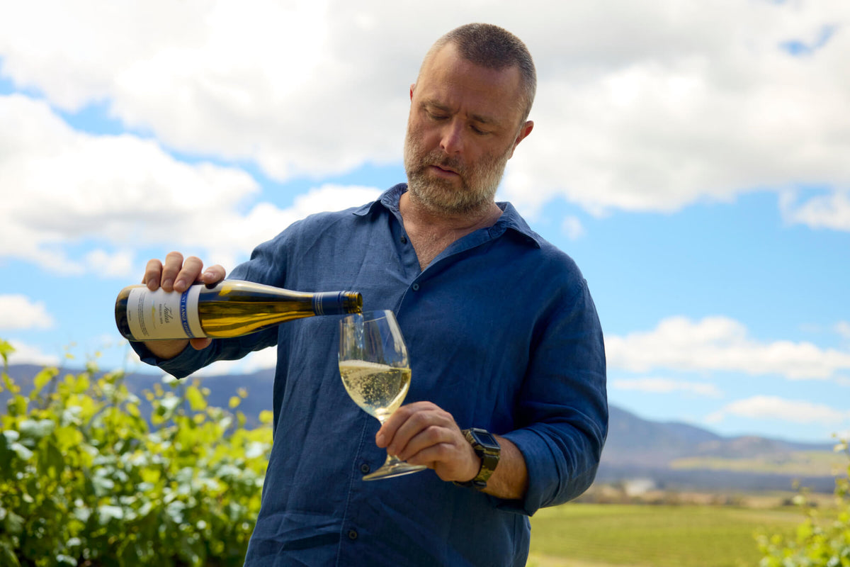 Man pouring white wine into a glass outdoors with vineyard views