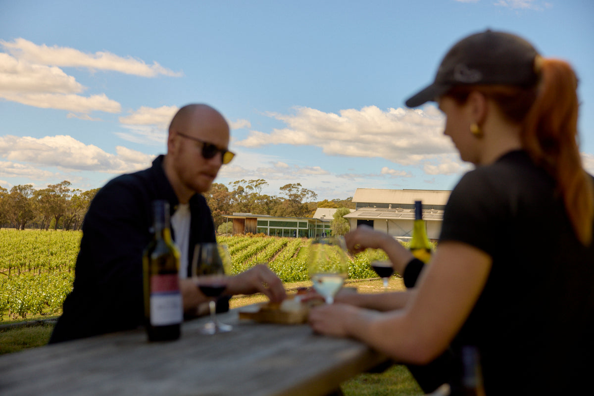 Guests tasting wine at an outdoor table overlooking the vineyard and winery