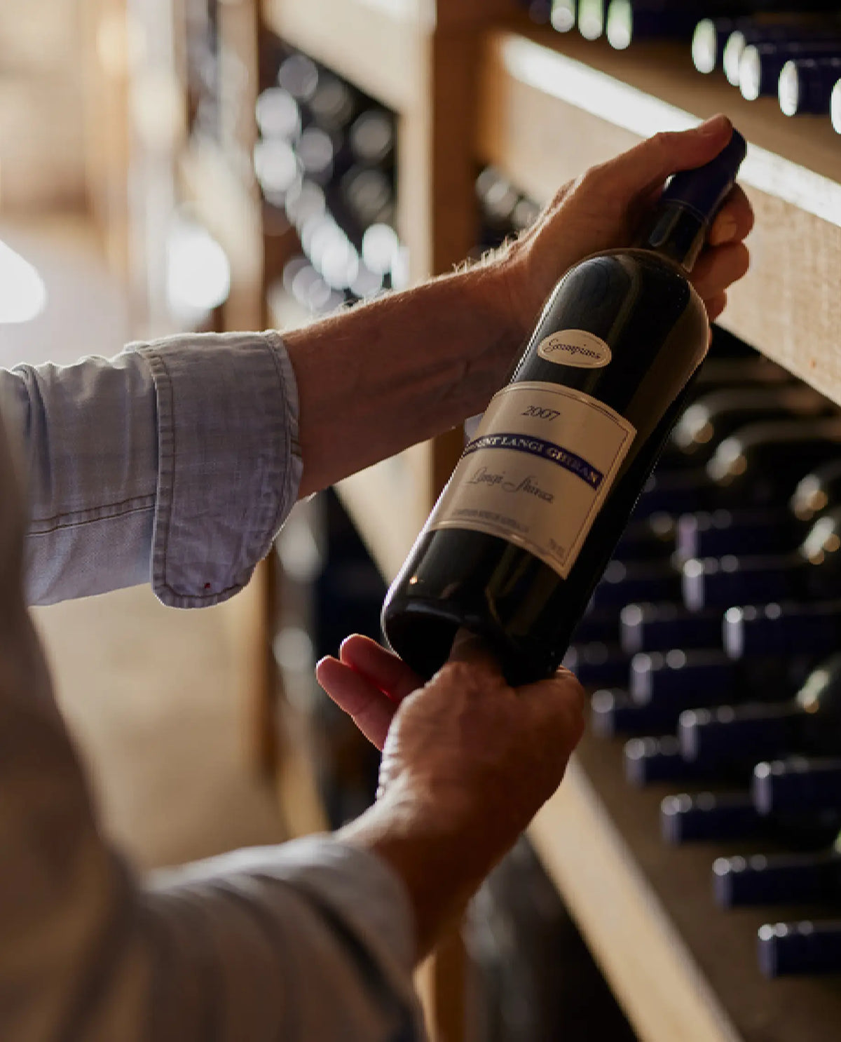Hands placing a bottle of Mount Langi Ghiran wine onto a cellar rack shelf