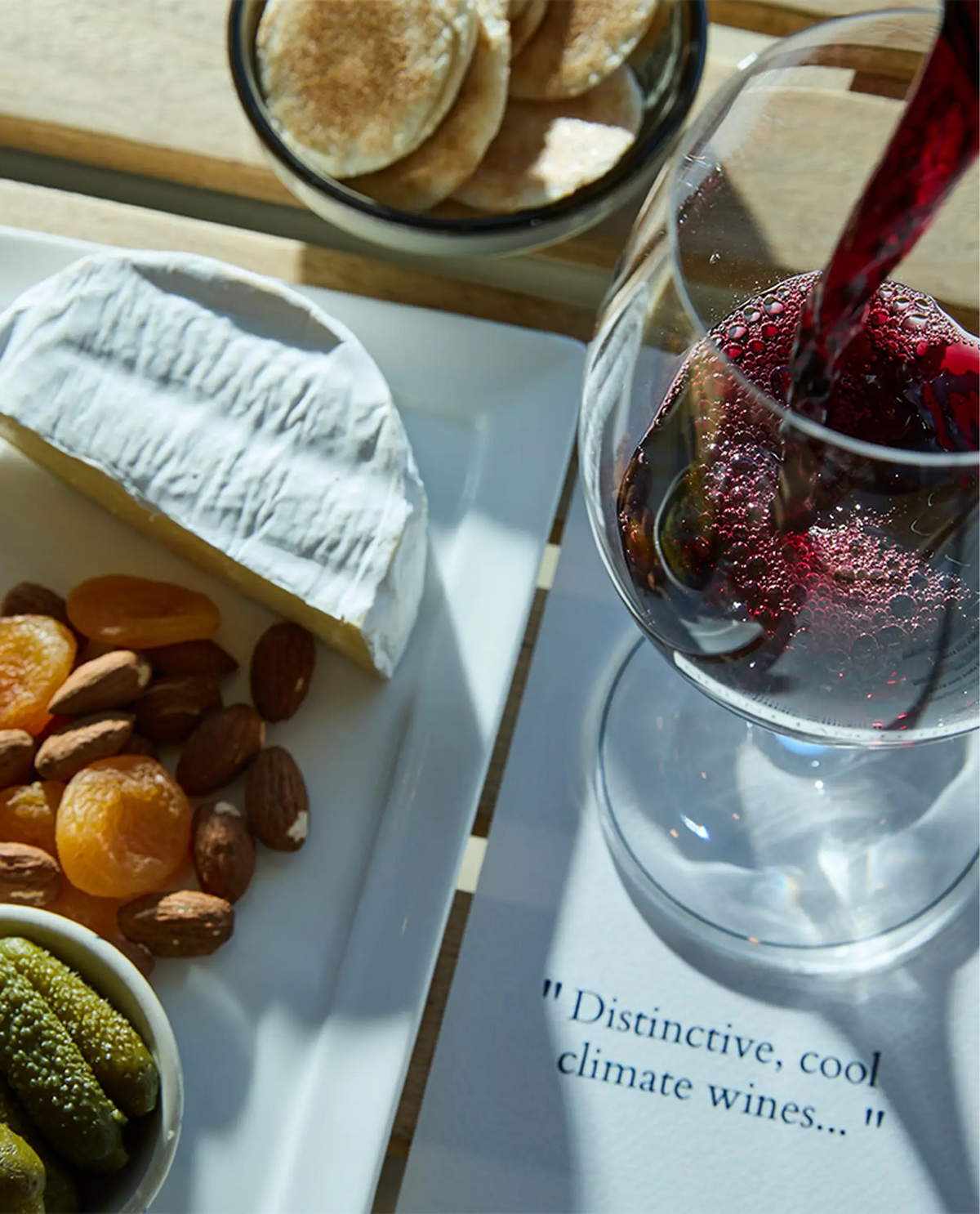 Red wine pouring into a glass beside a cheese and dried fruit platter