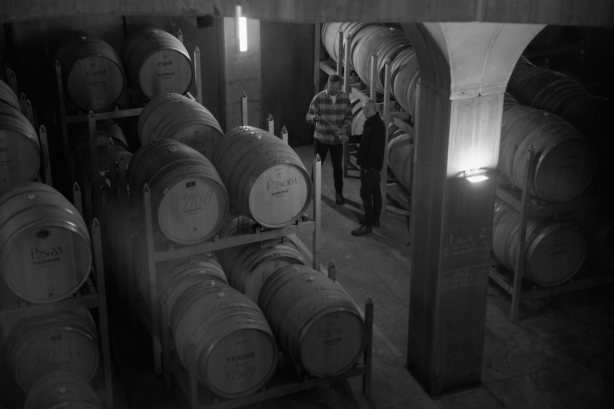 Black and white photo of two men examining wine in a barrel cellar