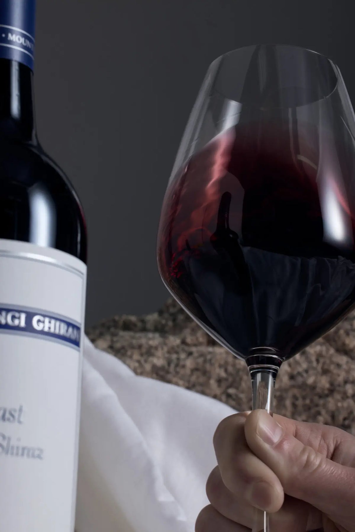 Close-up of a hand swirling a glass of red wine beside a Mount Langi Ghiran bottle