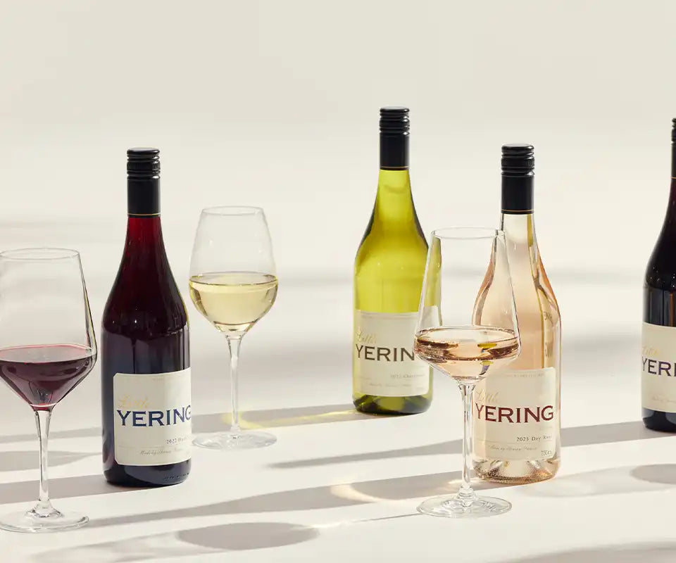 Row of Yering Station wine bottles and glasses of red, white and rose wine on a light background