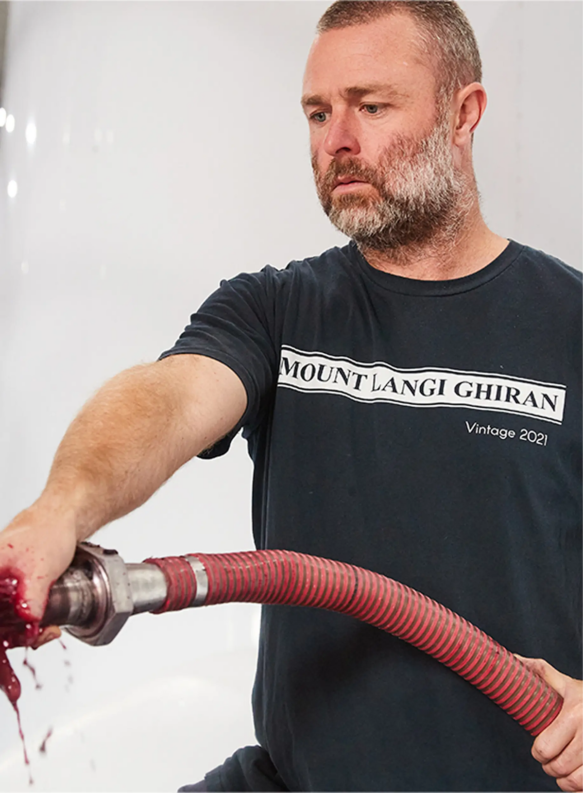 Man wearing a Mount Langi Ghiran Vintage 2021 t-shirt handling a hose with red wine dripping from the fitting
